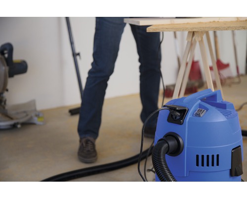 Dílenská scéna s vysavačem, pracovním stolem a řemeslníkem