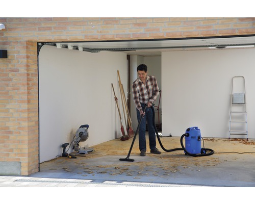 Muž vysává piliny v garáži průmyslovým vysavačem