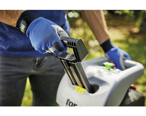 Osoba obsluhuje zahradní drtič s pracovními rukavicemi.