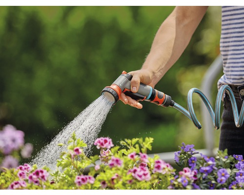 Osoba zalévá květiny zahradní stříkací pistolí Gardena.