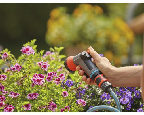 Zahradní scéna s osobou zalévající květiny zahradní stříkací pistolí Gardena.