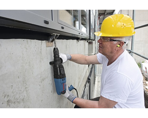 Řemeslník vrtá vrtacím kladivem otvor do betonové zdi