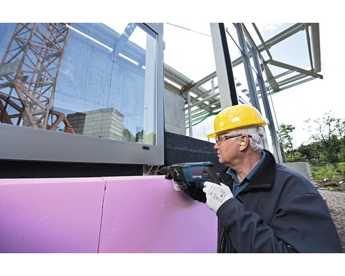 Řemeslník řeže izolační desku na budově pomocí šavlové pily.