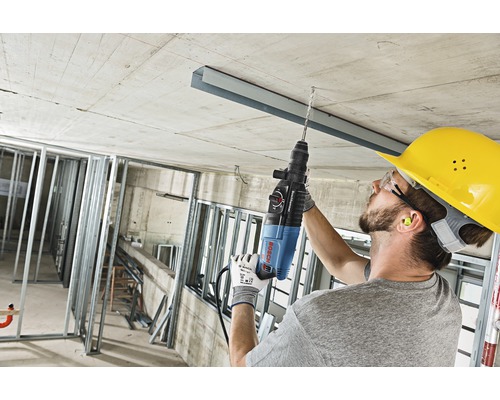 Řemeslník vrtá vrtacím kladivem do betonového stropu na staveništi.