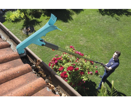 Muž čistí okap čističem okapů a odstraňuje listí.