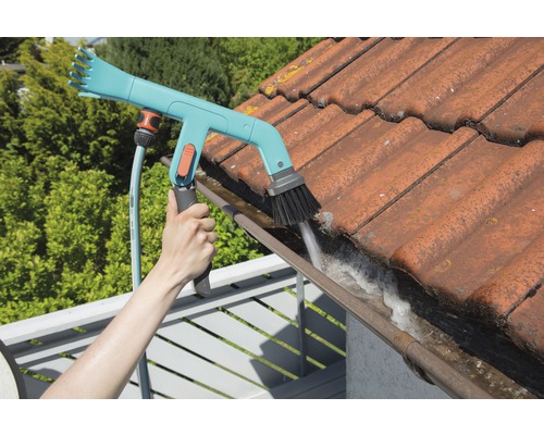 Osoba čistí okap pomocí kartáče na okapy a zahradní hadice.