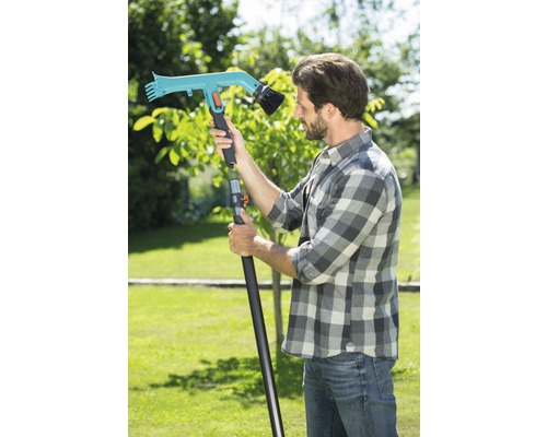 Muž se zahradním kartáčem s teleskopickou rukojetí na zahradě.