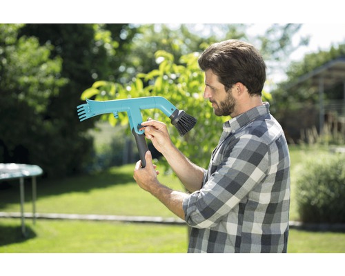 Muž obsluhuje kartáč na okapy na zahradě.