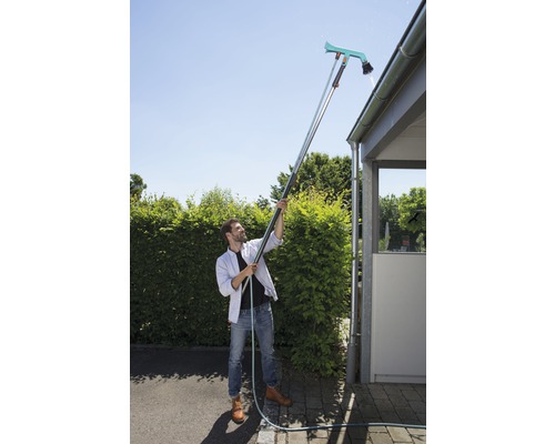 Muž čistí okap pomocí čističe okapů a teleskopické tyče.