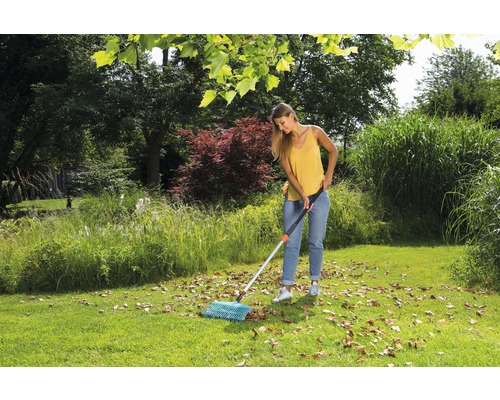 Žena zametá listí vějířovitými hráběmi na zahradě.