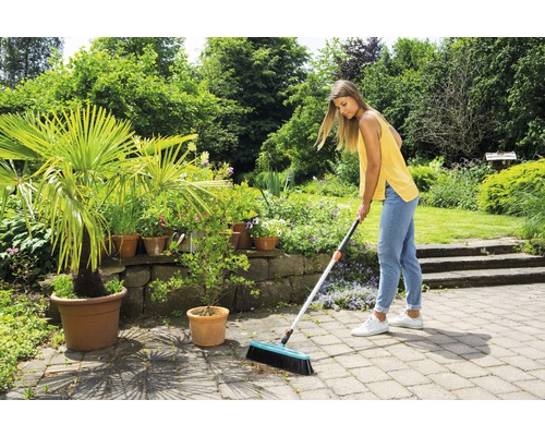 Žena zametá kamennou terasu koštětem na ulici v zahradě