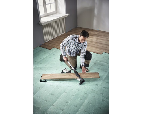 Muž pokládá laminát s řezačkou laminátu na kročejovou izolaci