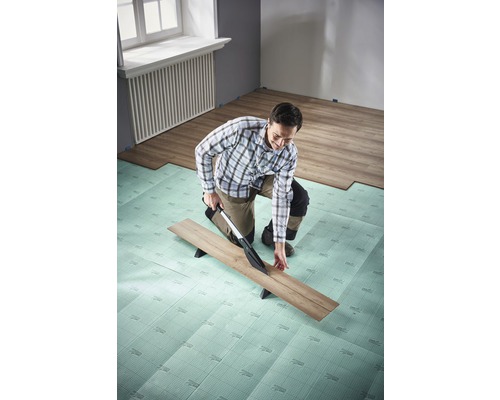 Muž řeže laminát pomocí řezačky laminátu na izolační podložce v místnosti