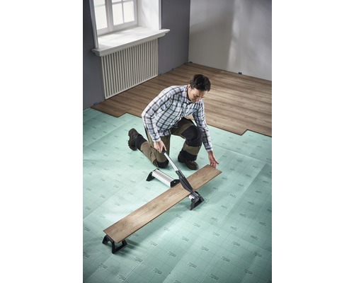Muž řeže laminát řezačkou laminátu na kročejové izolaci