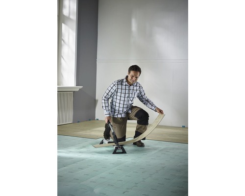 Muž pokládá laminát pomocí řezačky laminátu v místnosti.