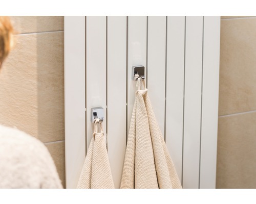 Bílý radiátor se dvěma ručníky a chromovanými háčky v koupelně.