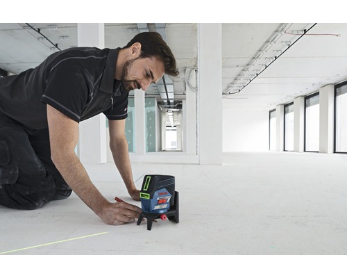 Muž používá křížový čárový laser Bosch na staveništi k nakreslení čáry na podlahu.