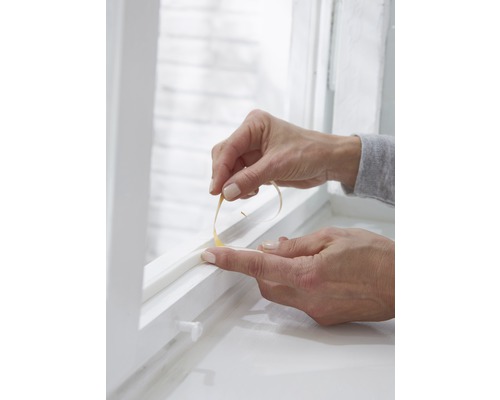 Osoba aplikuje těsnicí pásku na okno.