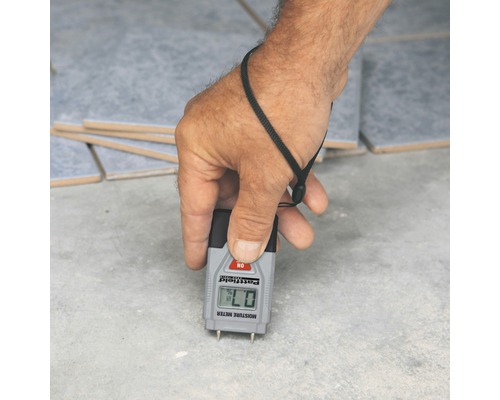 Ruka měří vlhkost podkladu vlhkoměrem.