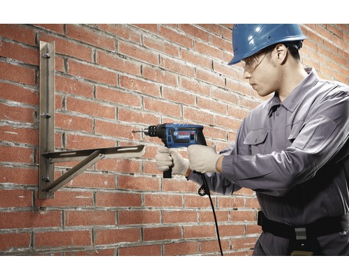 Řemeslník vrtá příklepovou vrtačkou do cihlové zdi