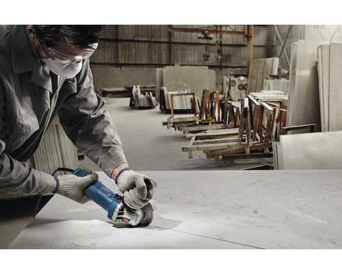 Pracovník s ochranou očí a úst používá úhlovou brusku pro zpracování kamenné desky v dílně.