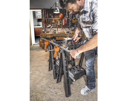 Muž řeže trubku na pracovní lavici se svorkami a ocaskou pilou v dílně.