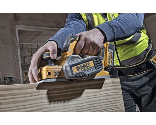 Osoba hobluje dřevěnou desku elektrickým hoblíkem. Hoblík je od společnosti DeWalt.