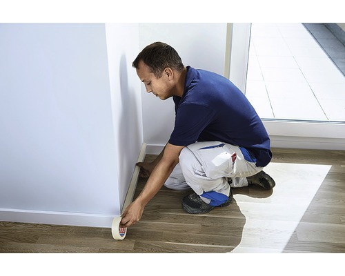 Muž lepí maskovací pásku na vnitřní stěnu