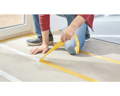 Osoba lepí lepicí páskou značku na podlahu.