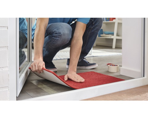 Osoba pokládá červenou rohožku před dveře.