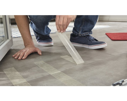 Osoba lepí pásku ze skelné tkaniny na dlaždicovou podlahu.