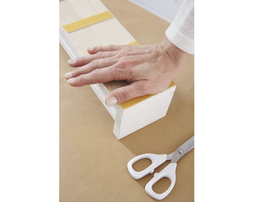 Ruka pevně tlačí na dřevěnou lištu s lepicími proužky, nůžky jsou připravené.