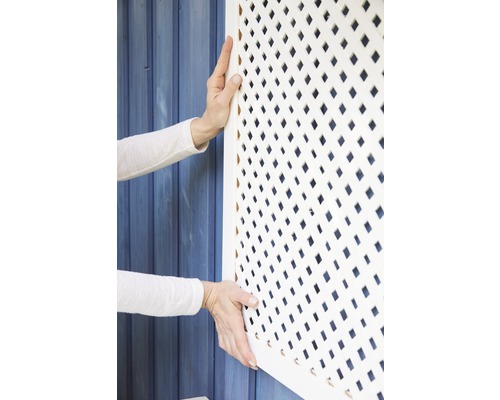 Osoba montuje bílý lamelový plotový prvek na modrou dřevěnou stěnu