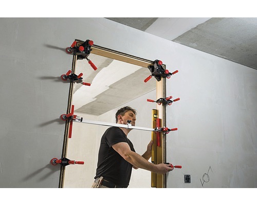 Muž montuje dveře do hrubé stavby pomocí šablony zárubně dveří.