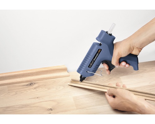 Osoba lepí ozdobné lišty tavnou lepicí pistolí.