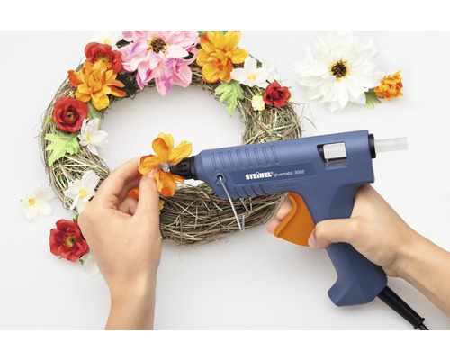 Osoba lepí květiny tavnou pistolí na věnec