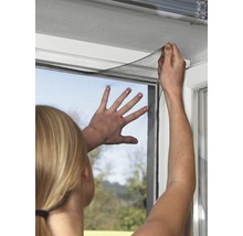 Žena připevňuje síť proti hmyzu na okenní rám.