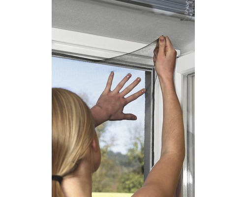 Žena připevňuje síť proti hmyzu na okenní rám.