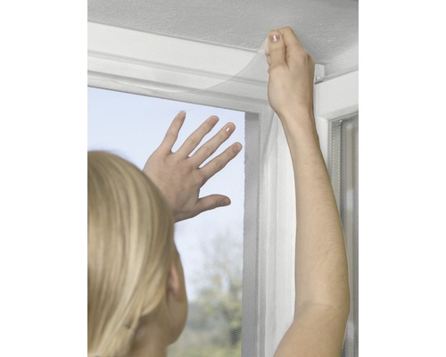 Osoba připevňuje síť proti hmyzu k rámu okna