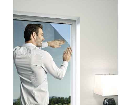 Muž aplikuje solární fólii na okno.