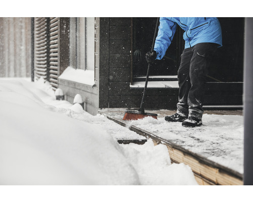 Osoba zametá sníh koštětem před vchodem do domu