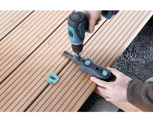 Osoba upevňuje terasové prkno pomocí šroubové svorky a akumulátorového šroubováku