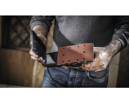 Muž drží vibrační brusku připravenou k práci.