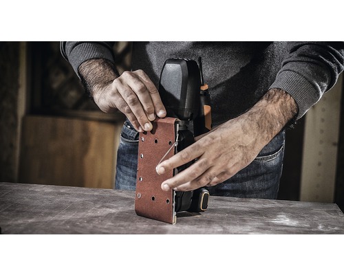 Osoba mění brusný papír na pásové brusce.