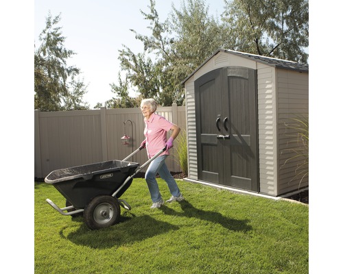 Žena tlačí kolečko na zahradě s kůlnou.