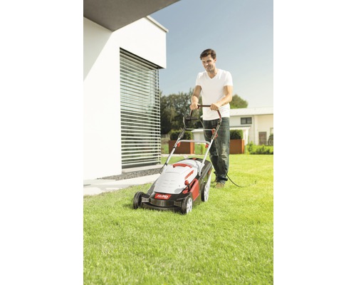 Muž seče trávník elektrickou sekačkou na zahradě.