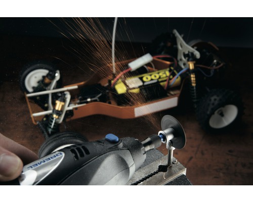 Logo Dremel. Osoba opracovává obrobek pomocí multifunkčního nástroje Dremel, odlétávají jiskry. V pozadí je vidět model auta.