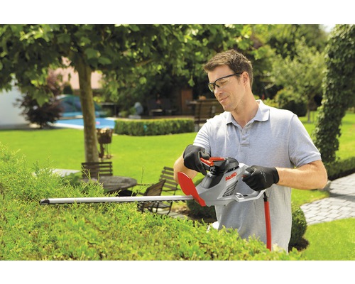 Muž stříhá živý plot nůžkami na živý plot na zahradě.