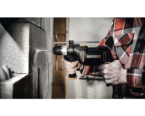 Osoba vrtá do cihlové zdi s příklepovou vrtačkou Worx.