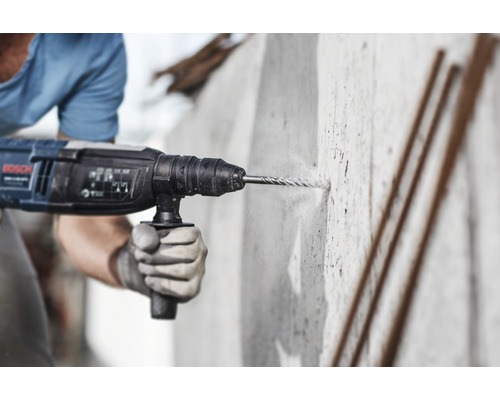 Muž vrtá díru do betonové zdi pomocí vrtacího kladiva